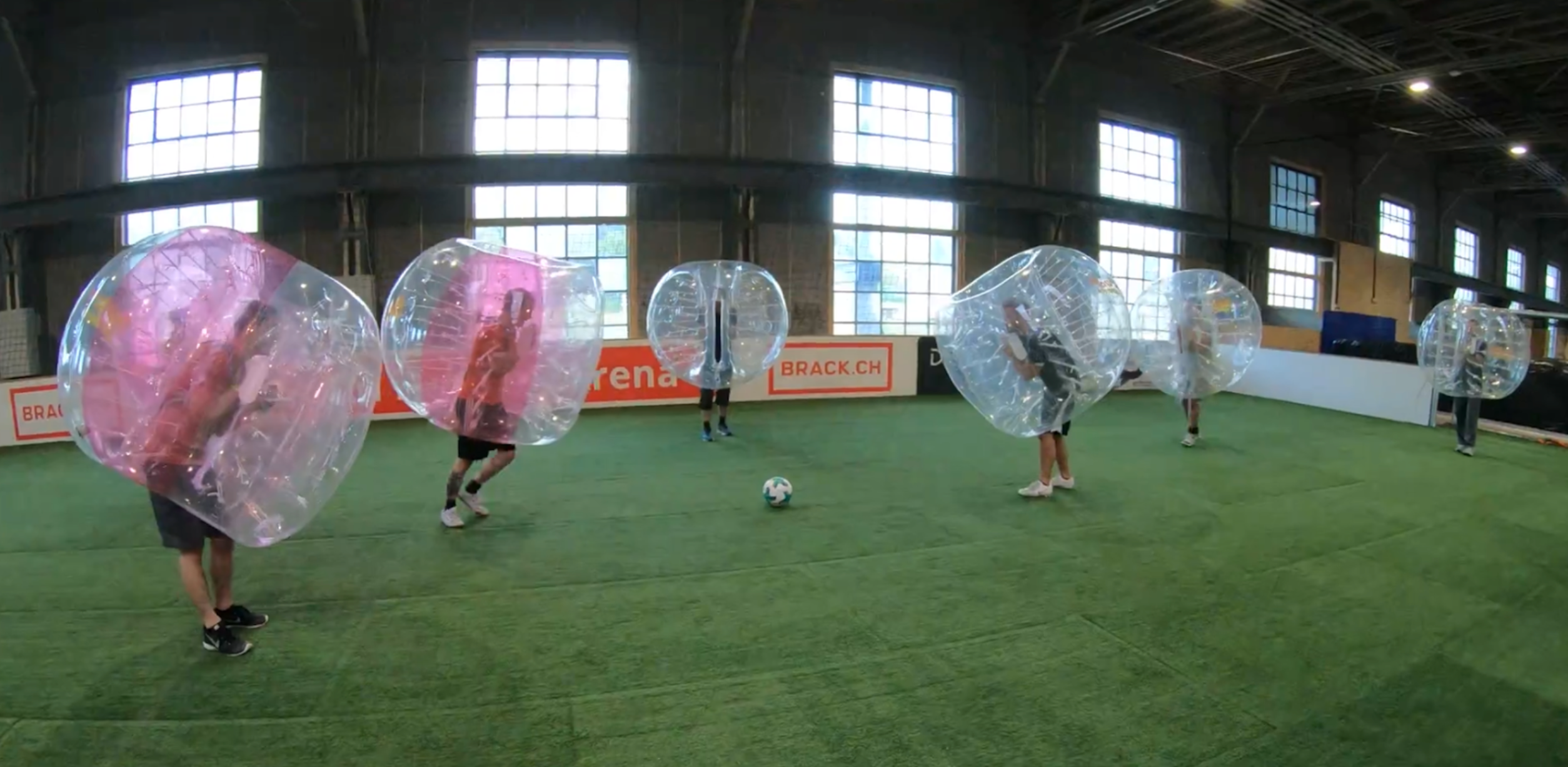 Fünf Personen spielen Bubble-Soccer in einer Halle.