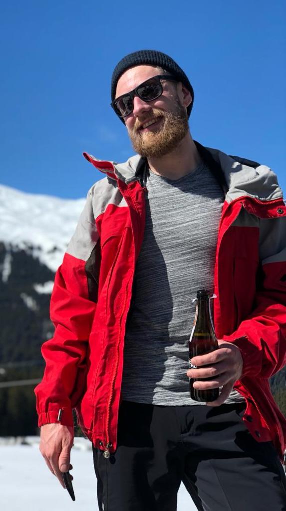 Ein junger Mann mit Skijacke, Sonnenbrille und einem Bier in der Hand.